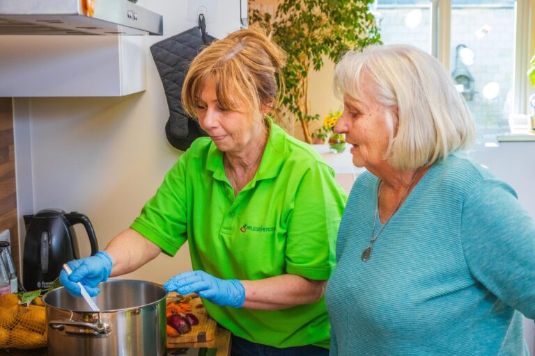 Betreuungskraft kocht gemeinsam mit einer Seniorin in der Küche